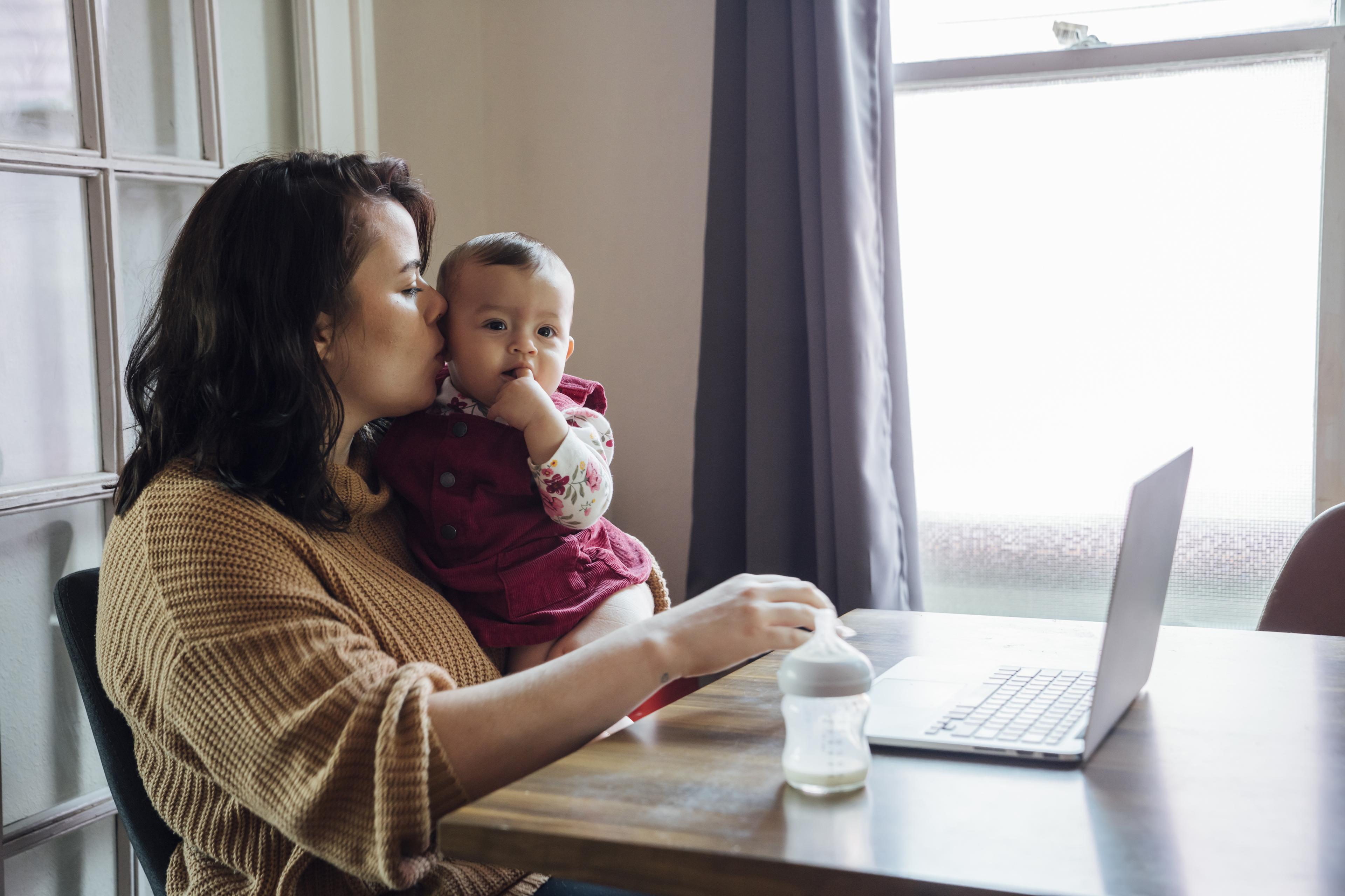woman holding baby while working on laptop