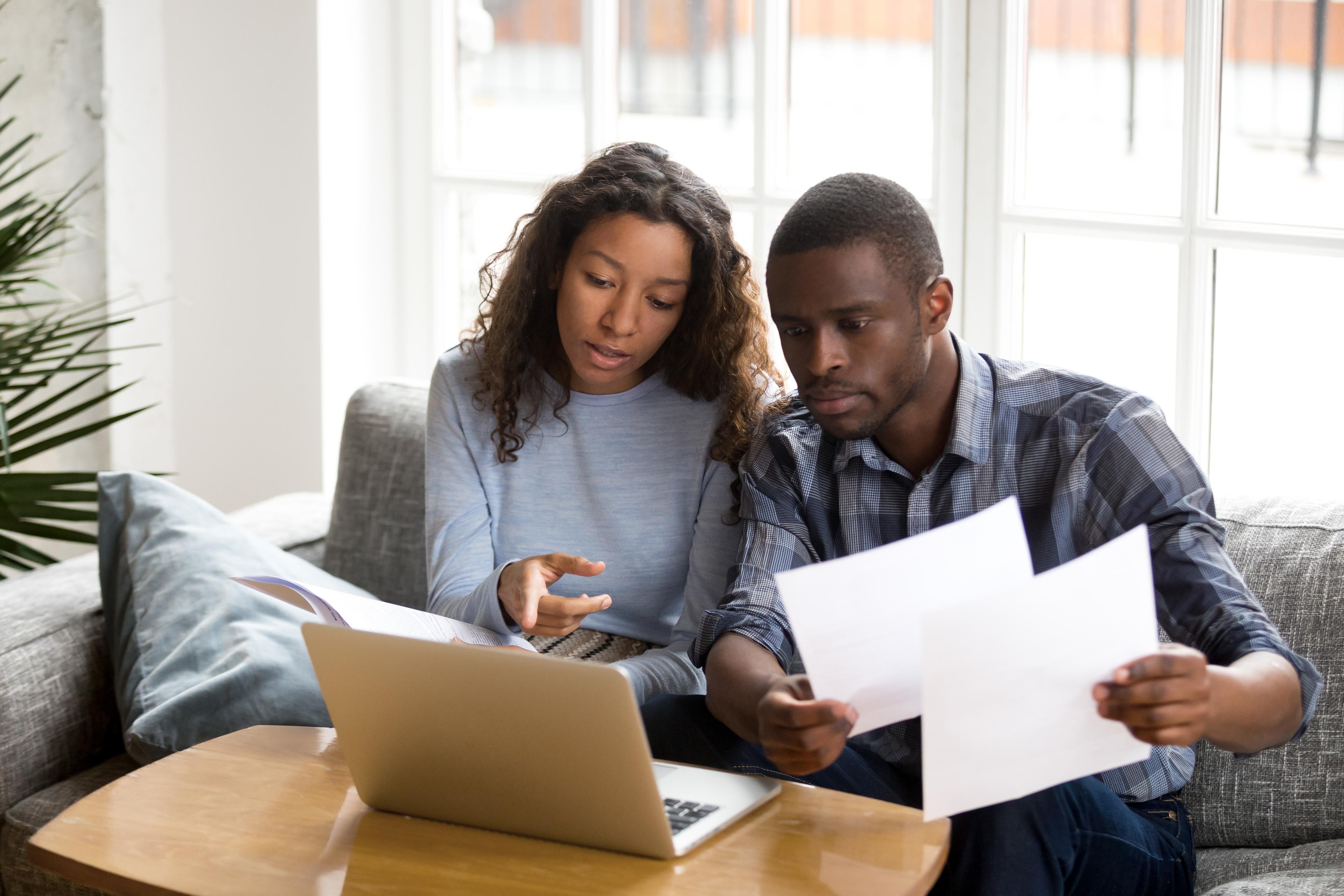 man and woman looking at laptop while holding papers